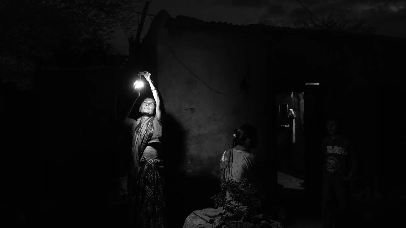 A lady fixing a light bulb outside her house in the darkness