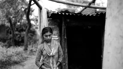 An Indian girl standing in front of her home which is a makeshift hut