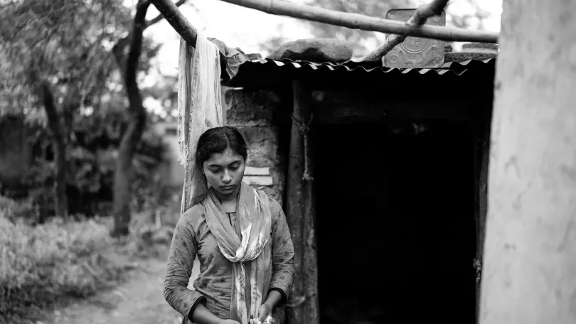 An Indian girl standing in front of her home which is a makeshift hut