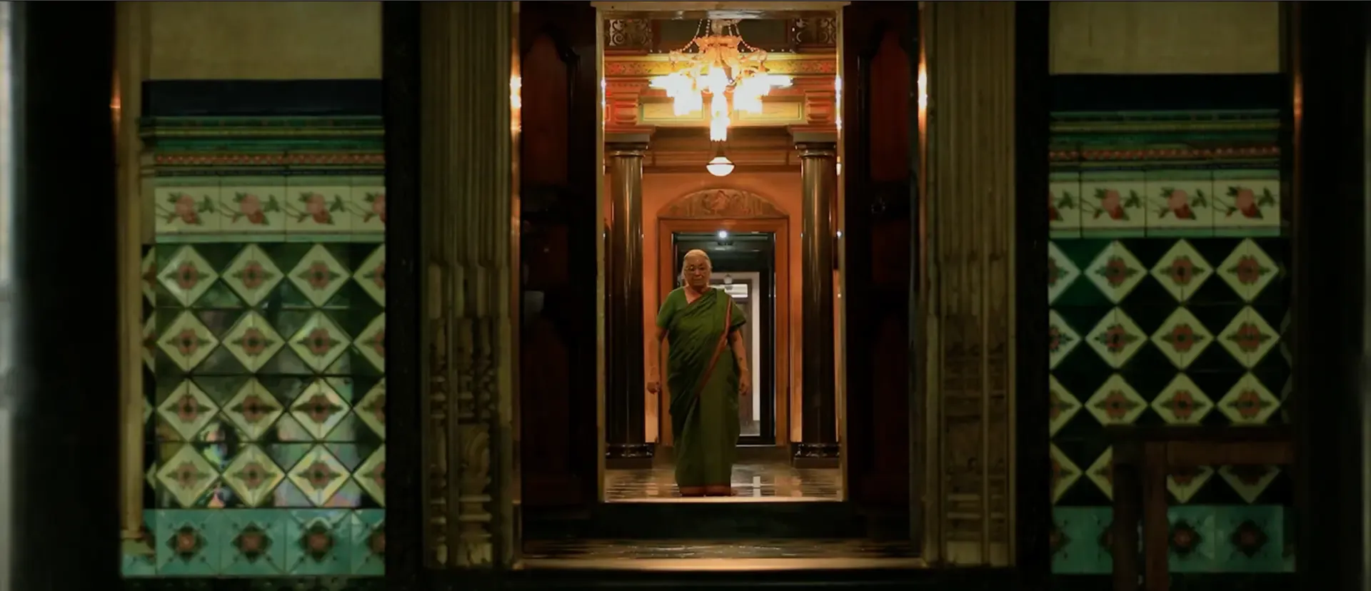An elderly indian lady in a saree standing in center of the doorway of her home