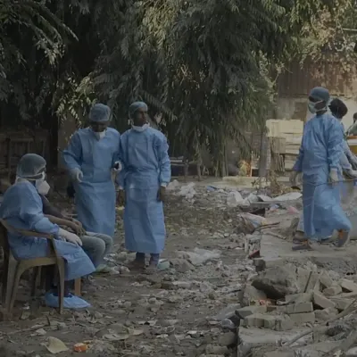 Covid-19 ambulance drivers sit on a trash strewn patch of concrete outside a cremation ground