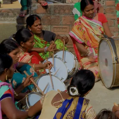 A group of indian women in sarees sitting on the ground playing the drums