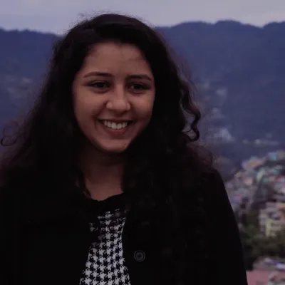 An indian lady smiling at the camera with mountains as her background