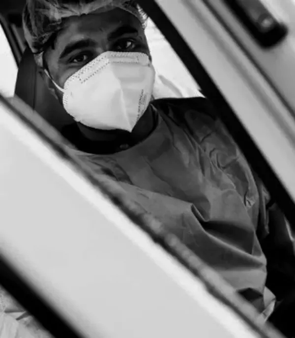 A healthcare worker in full personal protective equipment sitting in an ambulance